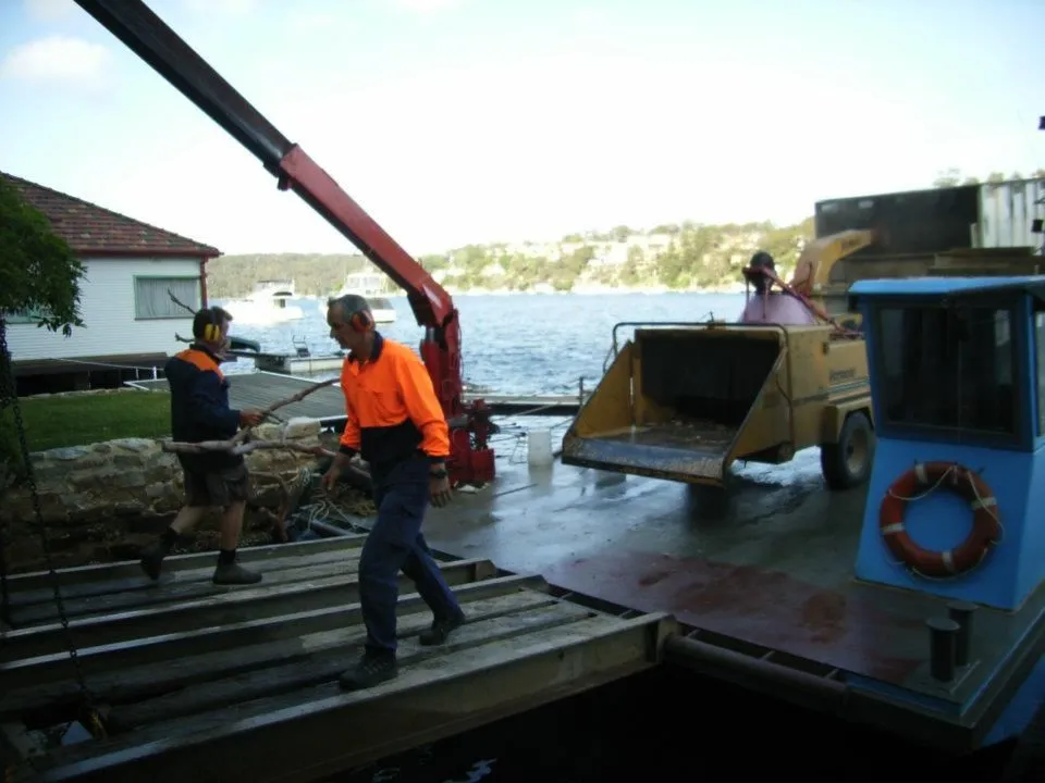 Crew members unloading a chipper and truck from a barge at a jetty
