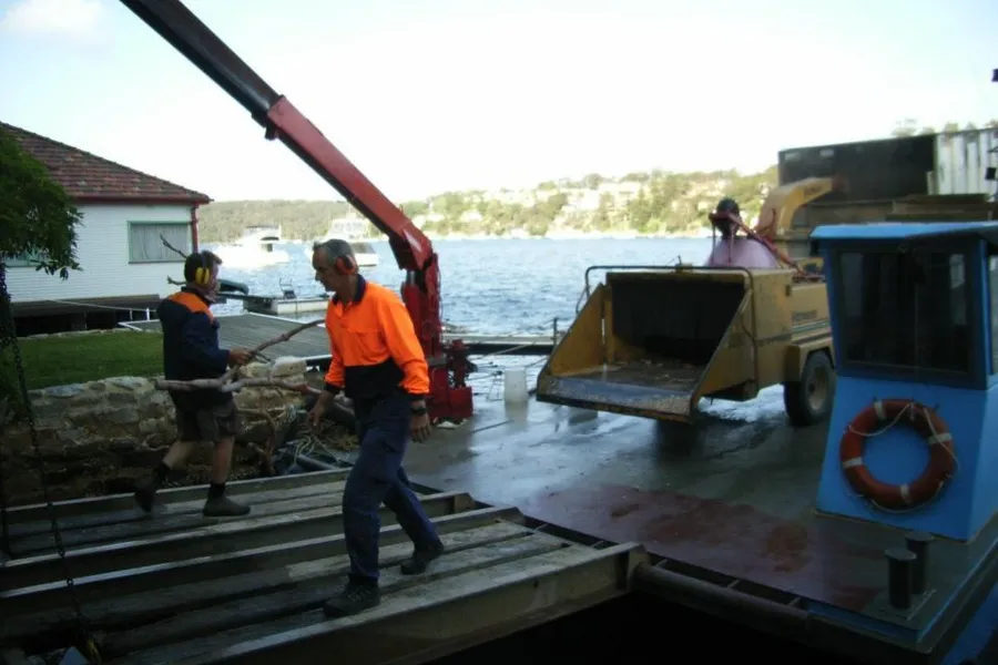 Crew members unloading a chipper and truck from a barge at a jetty