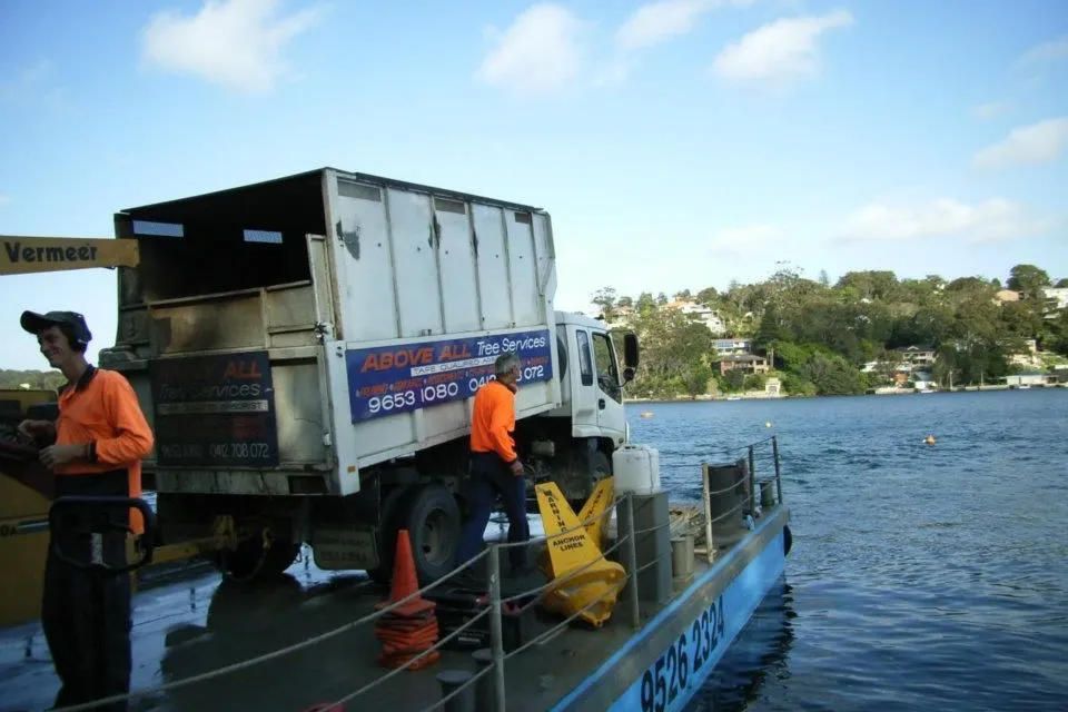 Truck and chipper on a barge beside a waterfront property